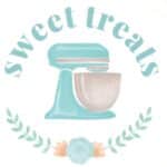 Watercolor illustration of a teal stand mixer framed by a circular wreath of green leaves and peach flowers on a white background